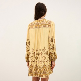 Model wearing Bash yellow mini dress with brown ornate print, long balloon sleeves and relaxed silhouette, rear view