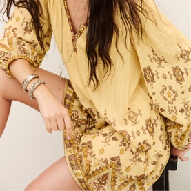 Model carrying Bash yellow printed mini bag with gold-tone hardware, styled with matching yellow floral print top and silver bracelets