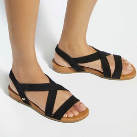 Model wearing Dune black elastic cross-strap flat sandals with tan footbed and slingback detail