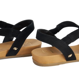 Dune black suede flat sandals with elasticated ankle strap, gold logo detail, and tan cushioned footbed, rear angle view.
