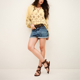 Model wearing Bash yellow embroidered boho top with denim shorts, lace belt, and brown strappy heeled sandals