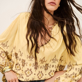 Model wearing Bash yellow blouse with ornate brown embroidery, balloon sleeves, styled with gold jewellery