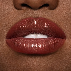 Model wearing MAC Lip Gloss in Damnsel, a deep reddish-brown shade with a glossy, high-shine finish on full lips.