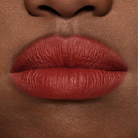 Model wearing MAC MACximal Silky Matte Lipstick in UnNatural Redhead, a warm muted brick-red matte shade on lips.