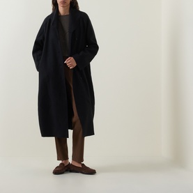 Model wearing Oska Fold-Down Wrap Coat in black; knit wool with balloon hem, styled with brown trousers and loafers.
