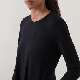 Model wearing Oska Solid Draped Dress in black, showing round neckline, long sleeves and fluid silhouette with centre front seam detail.