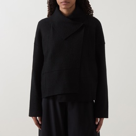 Model wearing Oska Fold-Down Wrap Jacket in black with asymmetric hem and fold-down collar, styled with wide-leg black trousers.