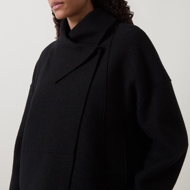 Model wearing Oska Fold-Down Wrap Jacket in black, featuring a fold-down collar, dropped shoulders, and asymmetric hem in knit construction.