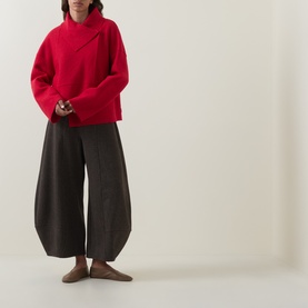Model wearing Oska scarlet wool jacket with asymmetric collar, styled with dark wide-leg trousers and brown loafers.