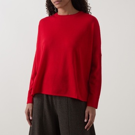 Model wearing Oska Rib-Knit Sweater in scarlet, crew neckline, dropped shoulders, long sleeves, styled with grey wide-leg trousers