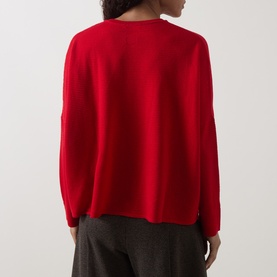 Model wearing Oska Rib-Knit Sweater in scarlet, shown from behind, with crew neck, dropped shoulders and long sleeves. Styled with grey trousers.