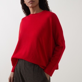 Model wearing Oska Rib-Knit Sweater in scarlet with crew neck and dropped shoulders, styled with grey tweed trousers.