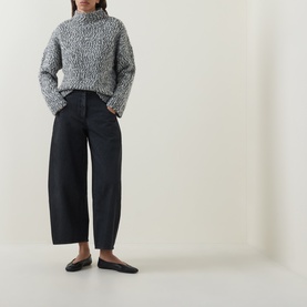 Model wearing Oska Chunky-Knit Sweater in black, mock neck, dropped shoulders, styled with wide-leg dark trousers and flat loafers.