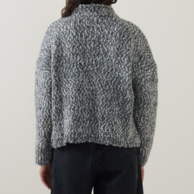 Model wearing Oska Chunky-Knit Sweater in black, rear view, mock neck, dropped shoulders, textured boucle knit, styled with dark trousers