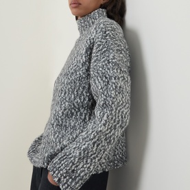 Model wearing Oska Chunky-Knit Sweater in black marl, featuring mock neckline, dropped shoulders, and textured chunky-knit finish.