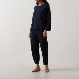 Model wearing Oska Solid Long-Sleeved Top in navy with crew neck and flared hem, styled with navy tapered trousers and tan flats.