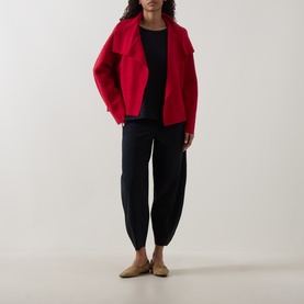 Model wearing Oska Solid Long-Sleeved Top in Navy, styled with a red wool jacket, tapered black trousers and tan mules.