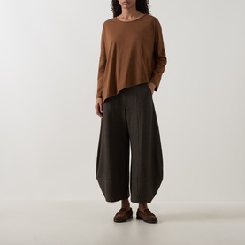 Model wearing Oska Asymmetric Long-Sleeved Top in Wood with round neck and asymmetric hem, styled with wide-leg dark trousers and brown loafers.