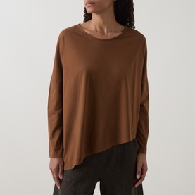 Model wearing Oska Asymmetric Long-Sleeved Top in Wood, with round neckline, dropped shoulders and asymmetric hem, styled with dark trousers.