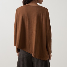 Model wearing Oska Asymmetric Long-Sleeved Top in Wood, showing back view with dropped shoulders and asymmetric hem, styled with dark trousers.