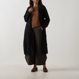Model wearing Oska Asymmetric Long-Sleeved Top in Wood, styled with a long black cardigan, dark wide-leg trousers and brown loafers.