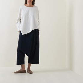 Model wearing Oska Asymmetric Long-Sleeved Top in ecru with round neck and asymmetric hem, styled with navy wide-leg trousers.