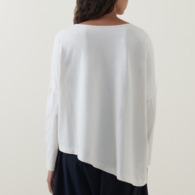 Model wearing Oska Asymmetric Long-Sleeved Top in ecru, showing back view with dropped shoulders, long sleeves and asymmetric hem. Styled with navy