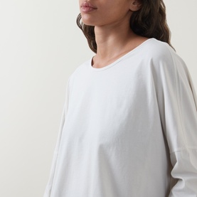 Model wearing Oska Asymmetric Long-Sleeved Top in ecru, featuring round neckline, dropped shoulders and long sleeves in soft cotton fabric.