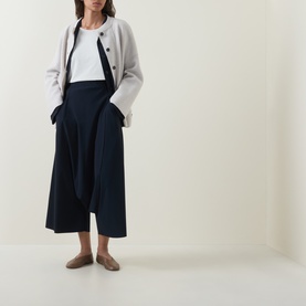 Model wearing Oska Asymmetric Long-Sleeved Top in ecru with navy wide-leg trousers, light grey jacket and brown flat mules.