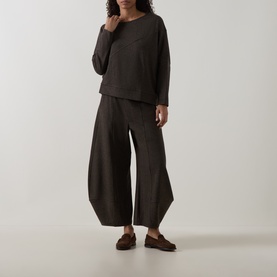 Model wearing Oska Asymmetric Knitted Sweater in Wood with matching wide-leg trousers and brown loafers.