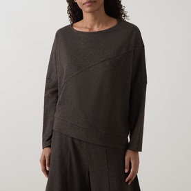Model wearing Oska Asymmetric Knitted Sweater in Wood with diagonal seam detail and crew neck, styled with wide-leg trousers.