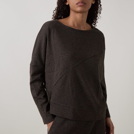 Model wearing Oska Asymmetric Knitted Sweater in Wood, featuring diagonal seam detail, crew neck, dropped shoulders, and long sleeves.