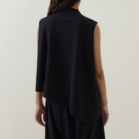Model wearing Oska black sleeveless top, shown from back, with asymmetric draped hem and high neck detail, styled with wide-leg black trousers.