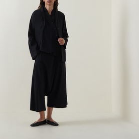Model wearing Oska black top with draped neckline, styled with wide-leg black trousers and black flat mules.