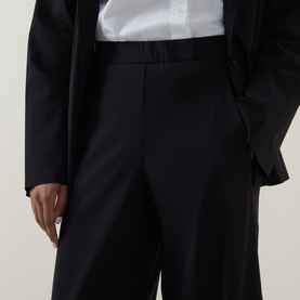 Model wearing Oska Straight Cropped Trousers in black with elasticated waistband, styled with a white shirt and black blazer.