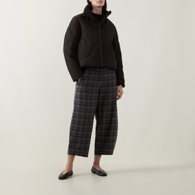 Model wearing Oska Choco check wide-leg cropped trousers, styled with a black puffer jacket and flat shoes.