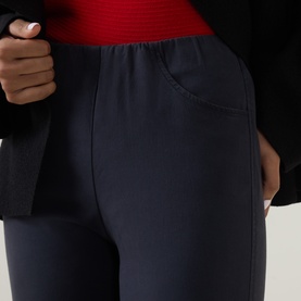 Model wearing Oska navy trousers, close-up showing elasticated waistband and front patch pocket, styled with red top and dark jacket.