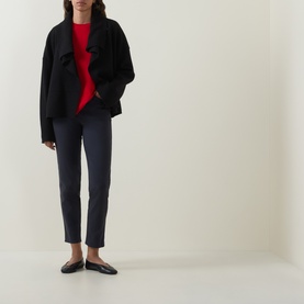 Model wearing Oska navy trousers with slim leg and ankle length, styled with black jacket, red top and black flat shoes.