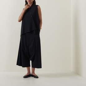 Model wearing Oska black wide-leg trousers with dropped crotch, styled with a sleeveless black top and black flat mules.