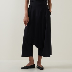 Model wearing Oska black wide-leg trousers with asymmetric hem and side pockets, styled with black slip-on flats.