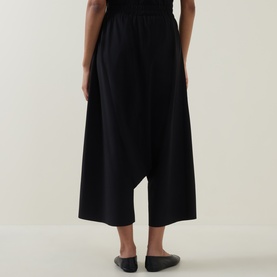 Model wearing Oska black wide-leg cropped trousers with elasticated waist, shown from behind, styled with black ballet flats