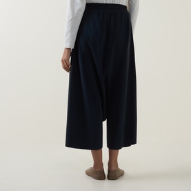Model wearing Oska Draped Wide Cropped Trousers in navy, rear view, styled with a white long-sleeve top and taupe flats.