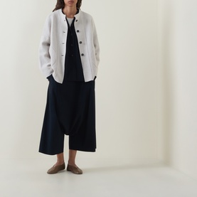 Model wearing Oska Draped Wide Cropped Trousers in navy with white linen jacket and tan flat shoes.