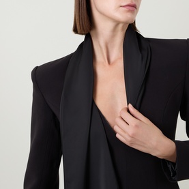 Model wearing Bardot black dress with deep V-neckline and satin scarf collar detail, structured shoulders visible.