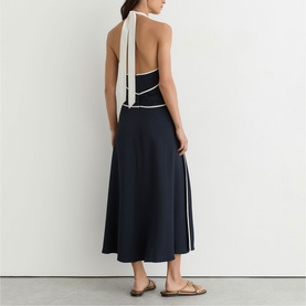 Model wearing Reiss blue halterneck midi dress with white contrast trim and open back, styled with gold flat sandals