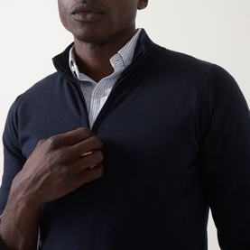 Model wearing John Smedley Tapton Extra Fine Knit Half-Zip Sweater in blue, styled over a striped shirt. Half-zip neckline detail shown.