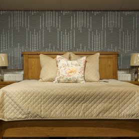 Fever + Hue Velvet Quilted Throw in Mocha draped over a double bed with cream pillows and floral cushion, grey feature wall behind.