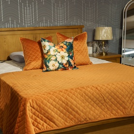 Fever + Hue Velvet Quilted Throw in Copper, styled on a bed with matching cushions and a floral accent cushion.