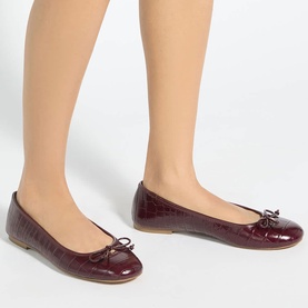 Model wearing Dune burgundy croc-effect ballet flats with bow detail and tan sole.