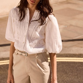 Model wearing Mint Velvet Dial Broderie Textured Blouse in white with puff sleeves, styled with beige belted trousers
